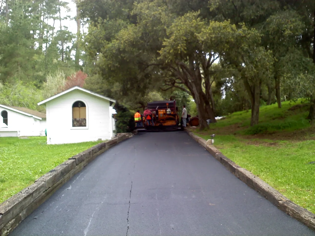 Crew paving a residential asphalt driveway through a wooded property